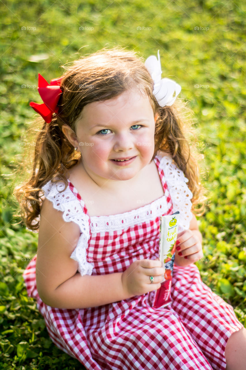 Young Girl in red and White Dress Eating Buddy Fruit Tube