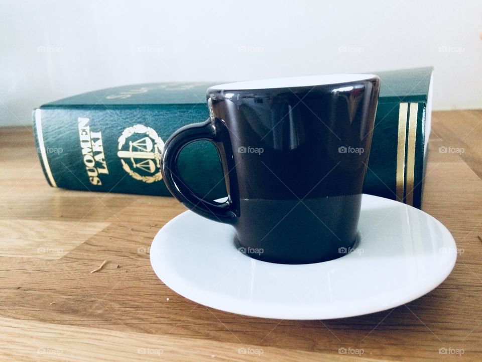 A cup of coffee and a Finnish law book on a wooden table