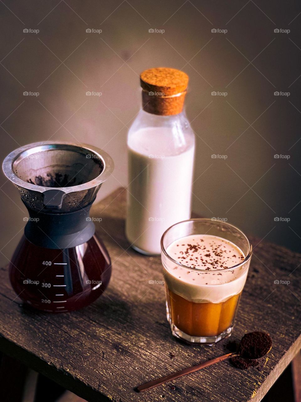 A cup of cafe latte, a bottle of milk and coffee dripper on a small wooden table