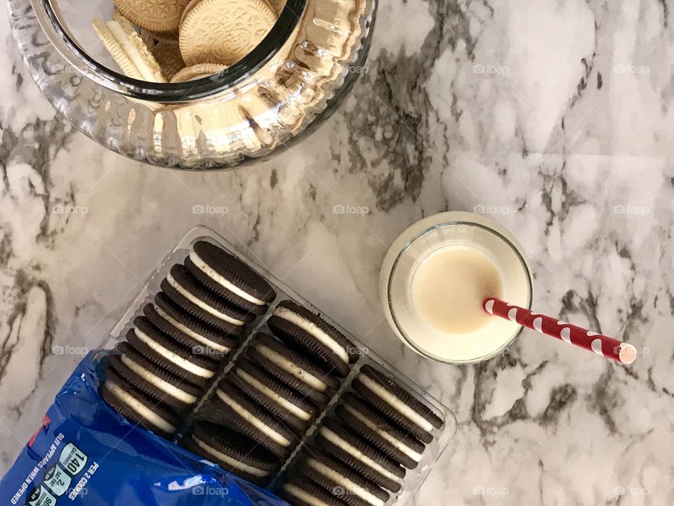 Double stuff Oreo chocolate cookies and golden double stuff Oreo cookies and a glass container of milk with a red and white straw Flatlay