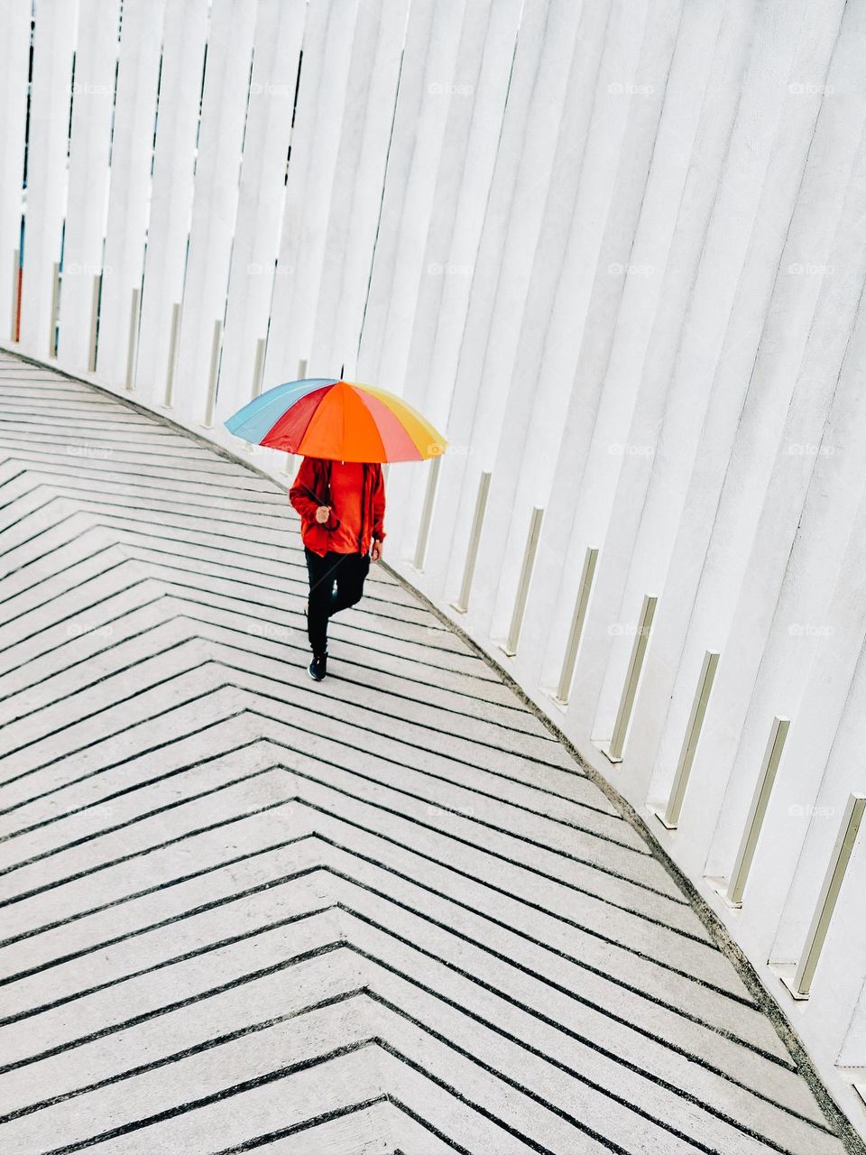 A man with a colorful umbrella walking down a concrete ramp