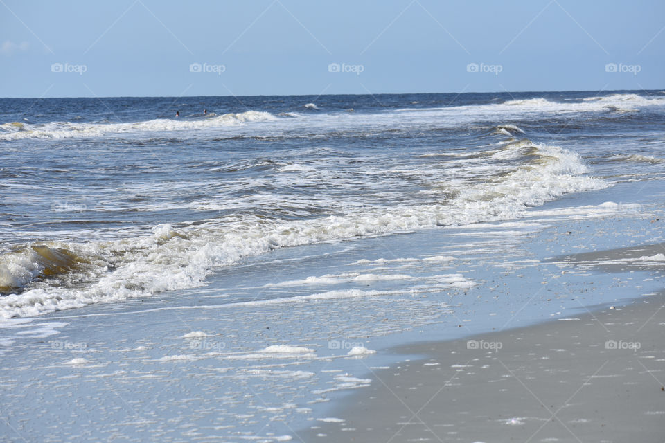 ocean waves crashing on beach shore. light brown sand. clear blue sky. Atlantic ocean myrtle beach south Carolina