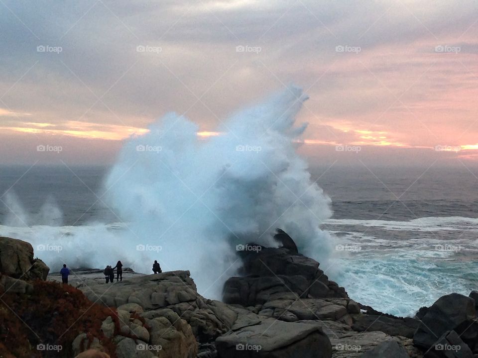 The beauty of danger!. Beautiful waves crushing onto the rocks while some people are watching the moment