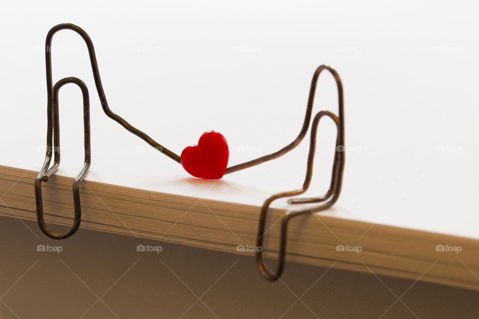 paper clips with heart symbolizing a person sitting on a stack of white paper. love concept