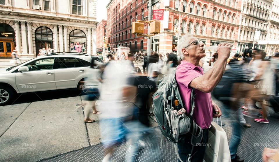 Older man drinking on busy street