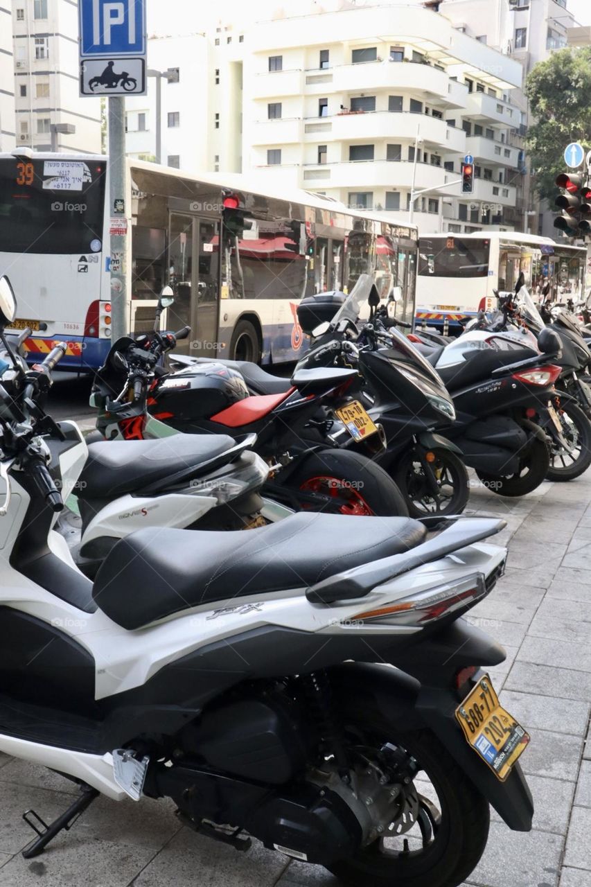 Many motorcycles parking on the street with buses drive on background 