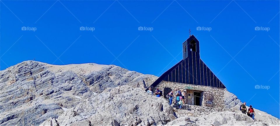 Beneath the blue sky on the “Zugspitze”, Germany’s tallest peak in the “Alps” at 2962 m we find the “Mariä Heimsuchung”, “Visitation of Mary” chapel inaugurated by “Cardinal Ratzinger”, later “Pope Benedict XVI” in 1980. 2024. Hypnotic Productions