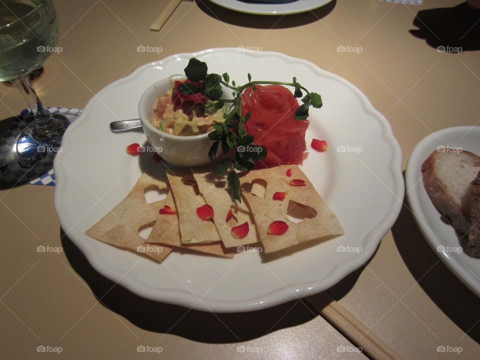 tomato and cheese Italian bruschetta with red rose shaped garnish, green garnish. served with crisp breads shaped like playing cards with heart suits and real rose petal garnishes. all on a white plate with beige table background.