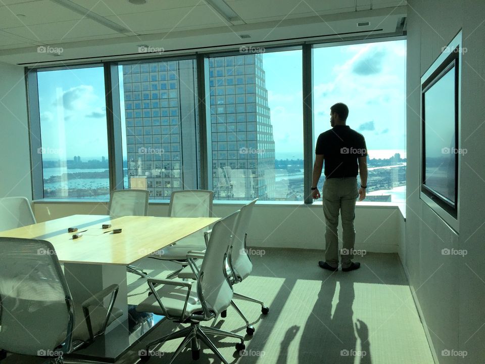 Success. Young man standing by panoramic window of office looking outside