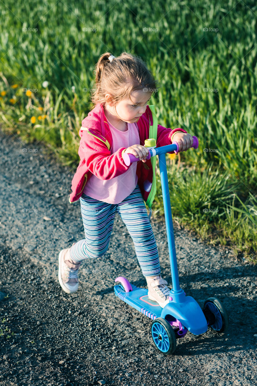 Little adorable girl having fun riding on scooter, playing outdoors. Real people, authentic situations