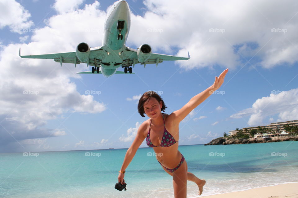 Airplane flying over woman outstretching her hand at beach