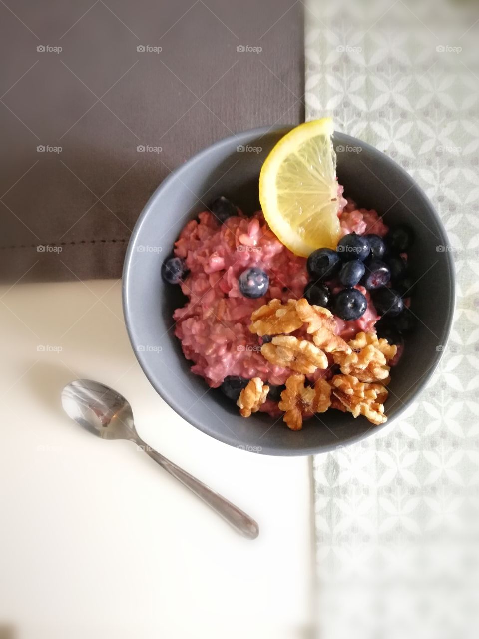 Breakfast bowl with pink oat meal, nuts and blueberries with a lemon slice and a spoon