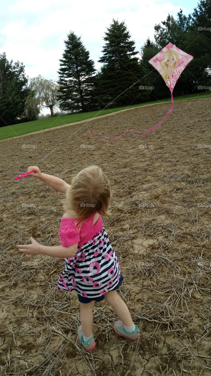 Little girl flies a Barbie kite in a field in early spring time on a windy day.