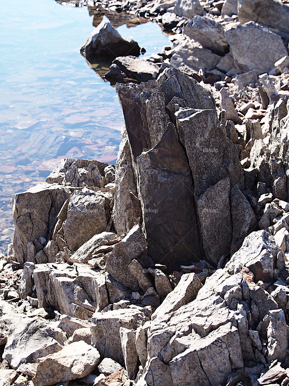 Jagged rocks and boulders along the shoreline of Ochoco Lake in Central Oregon on a sunny spring day.