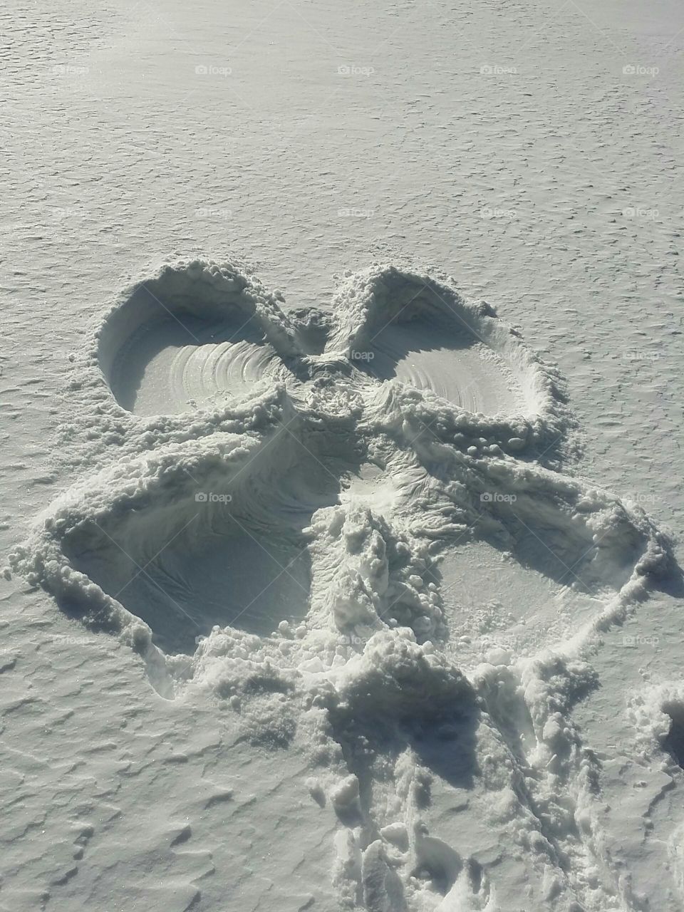 Snow angel made by a women on a lake on a sunny winter day