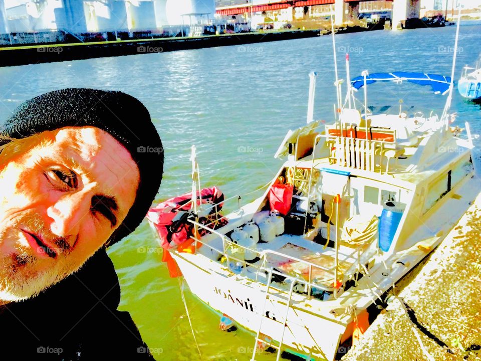 Sailor Timothy Trespas at Newtown Creek in Long Island City, Queens, New York on the shore at low tide with our boat “Salvation “ in the background. 2019. Hypnotic Productions