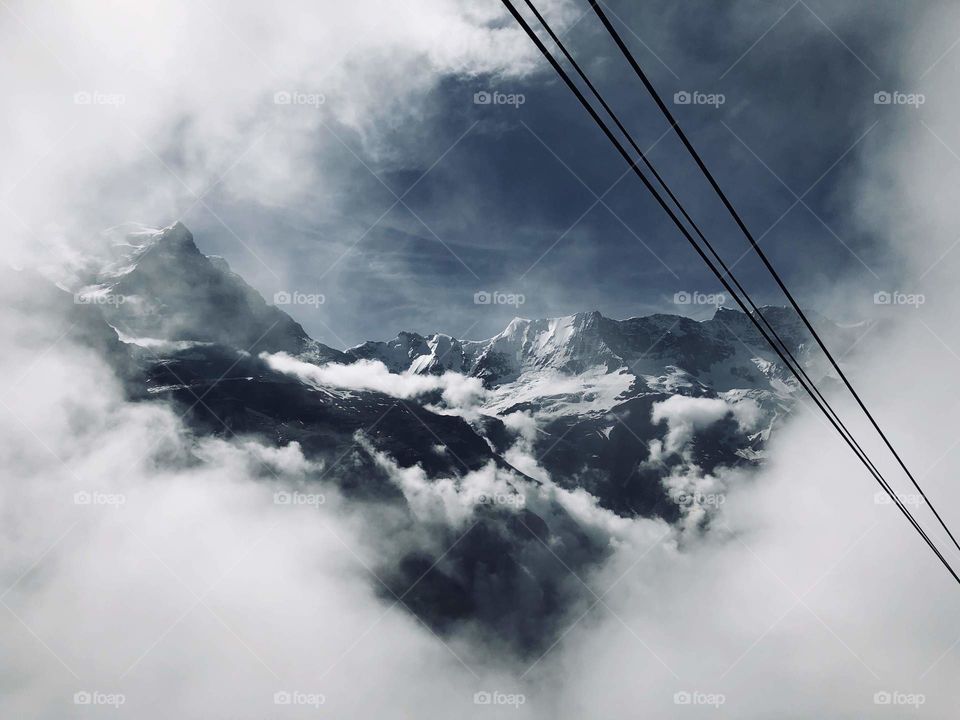 Cloudy, cool mountain top seen in Switzerland on the way up via a cable car. Cables can be seen in the picture, a breathtaking view that captures my heart in awe every time I see it. Everyone deserves to see this beautiful scenery once in their life.