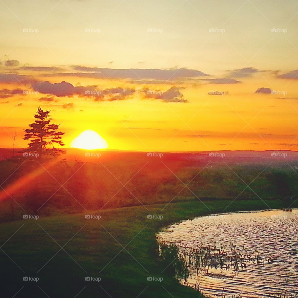 A small lake reflecting the sunset with rolling hills