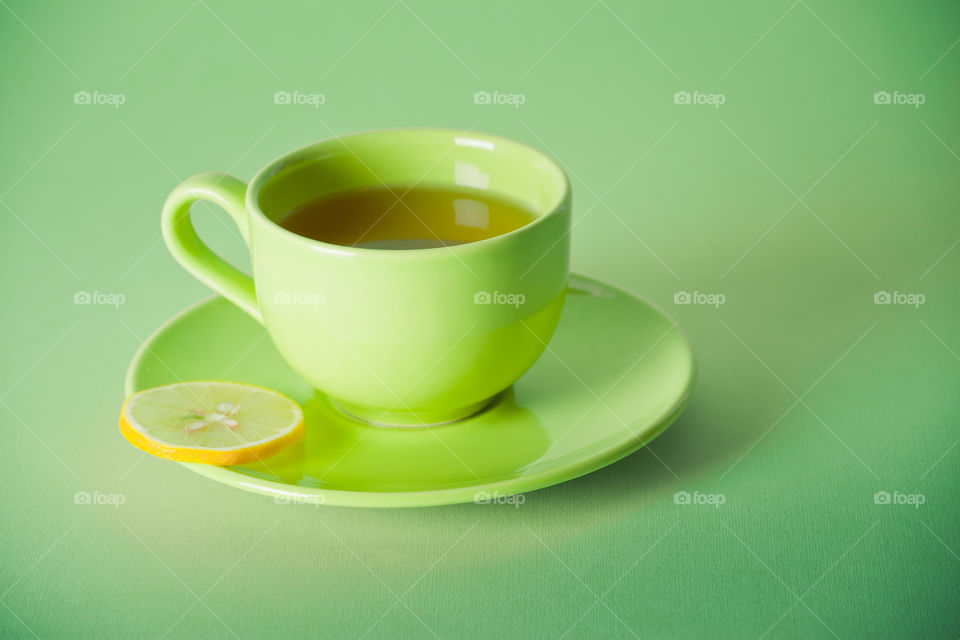 Green cup of green tea with lemon on green background