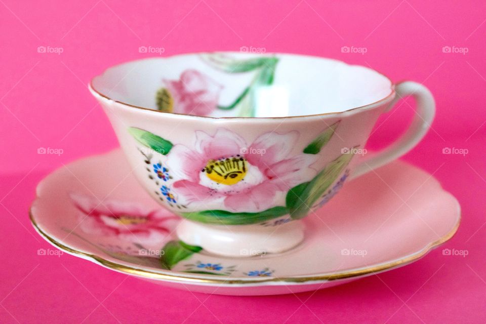 An antique hand-painted floral teacup on a bright pink background 