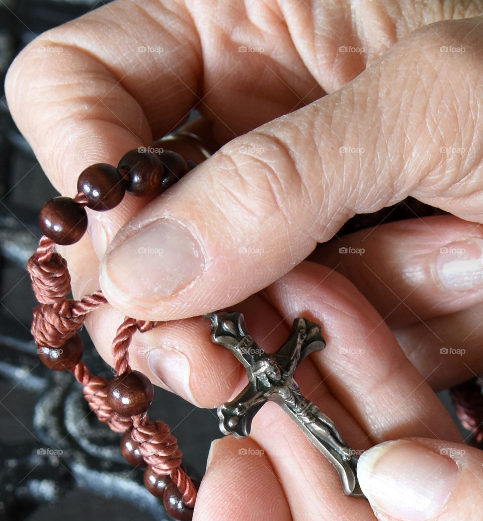 Praying while holding rosary beads with a crucifix attached.