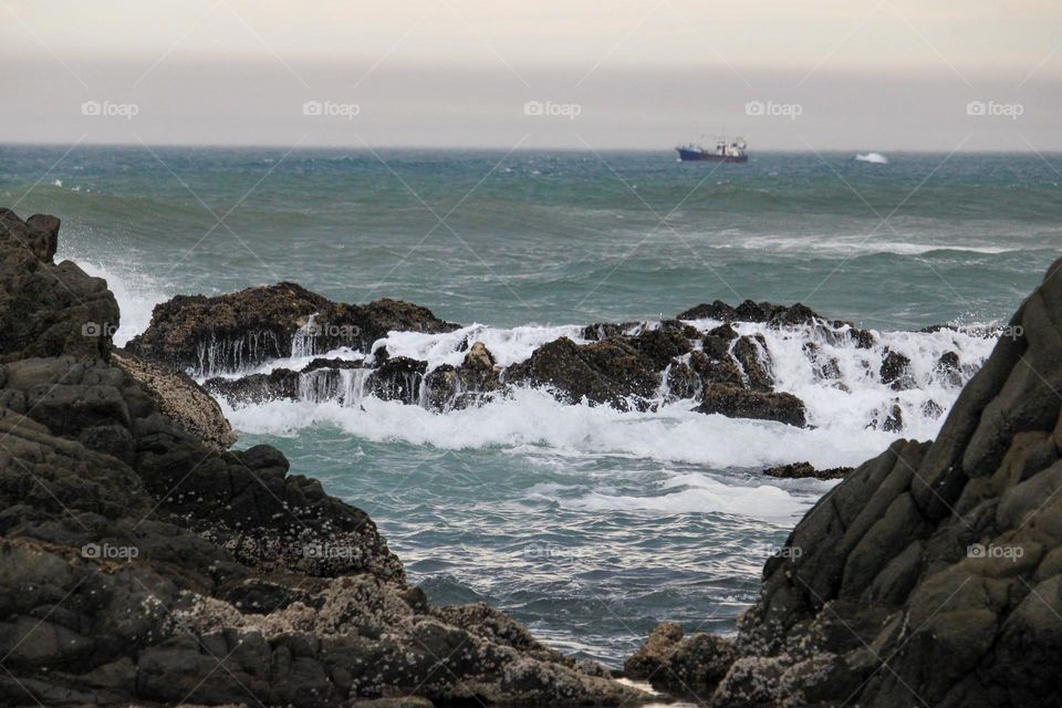 Waves crashing over the rocks with a boat in the distance