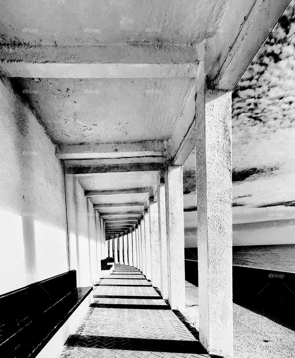 Black and white image of an open walkway with a colonnade of pillars vanishing into the distance with distinctive cloud formations