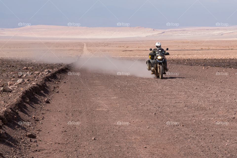 Motorcycle on gravel road. Motorcycle riding on a gravel road in Atacama desert, Chile. Dry, barren landscape. Dust follows motorcycle