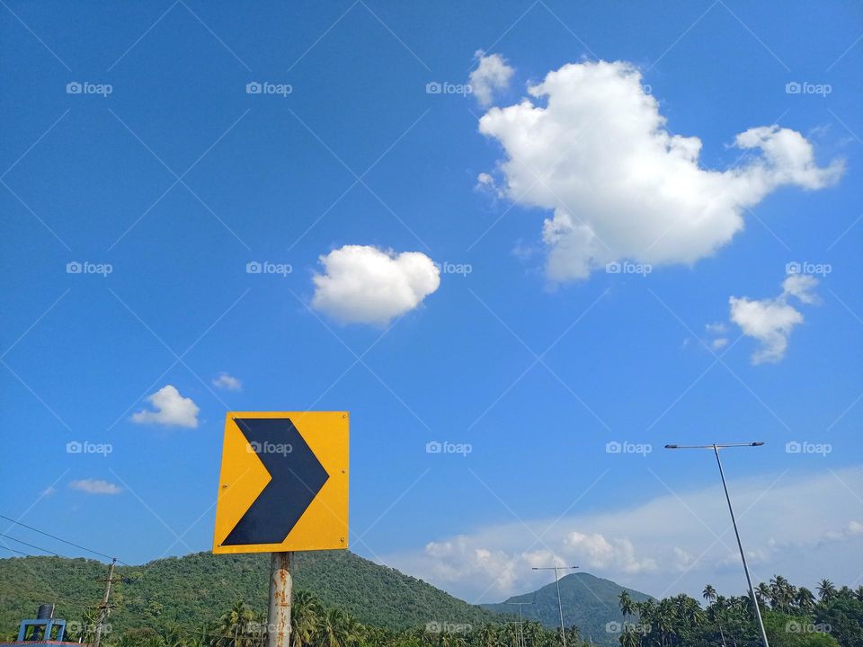 Black Arrow on yellow traffic sign with nice background blue sky clouds and green colour beautiful mountain