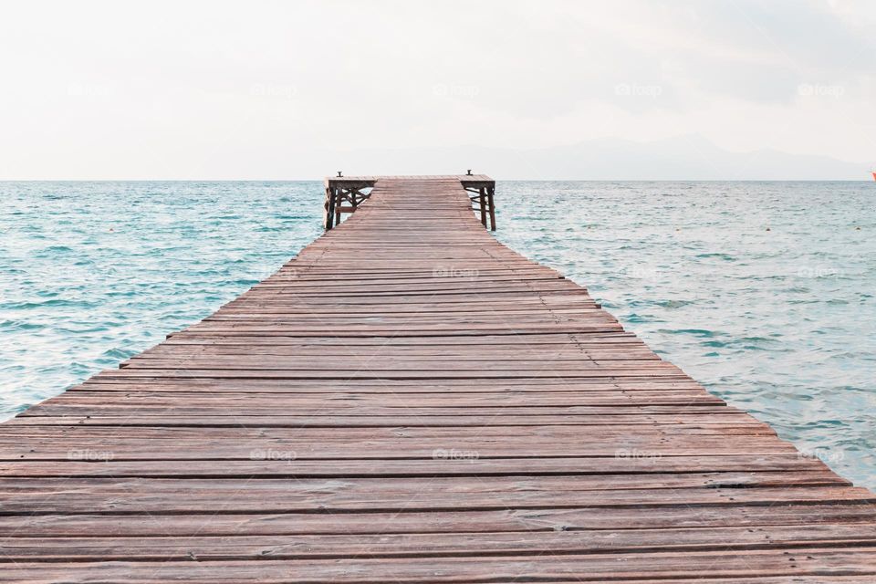Wooden jetty in the ocean leading to the horizon 