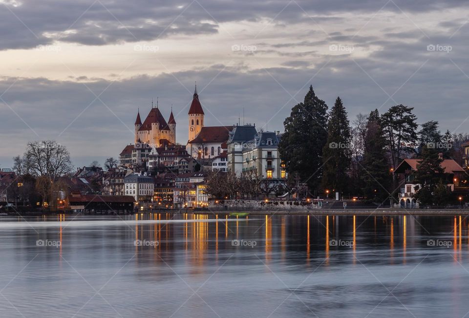 City lights of thun old town with castle and church reflected in aare river at twilight.