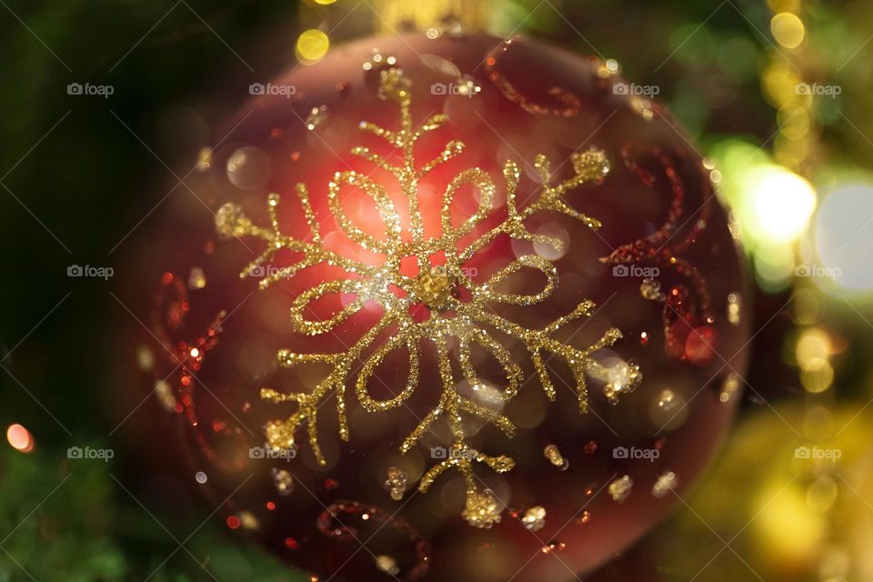 A portrait of a red and gold christmas ball with golden bokeh balls around it hanging in a xmass tree.