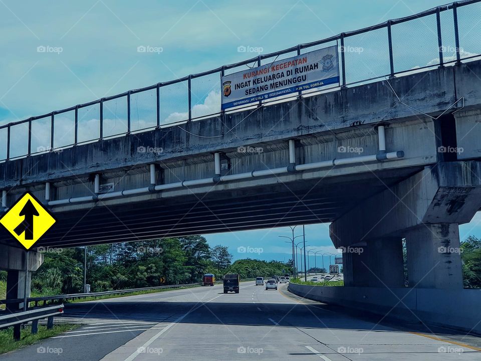 Driving on the toll road, Bandung city Indonesia, toll overpass, two-lane into one lane, toll road traffic sign, the basic color of the sign is yellow, and the lane direction sign is back