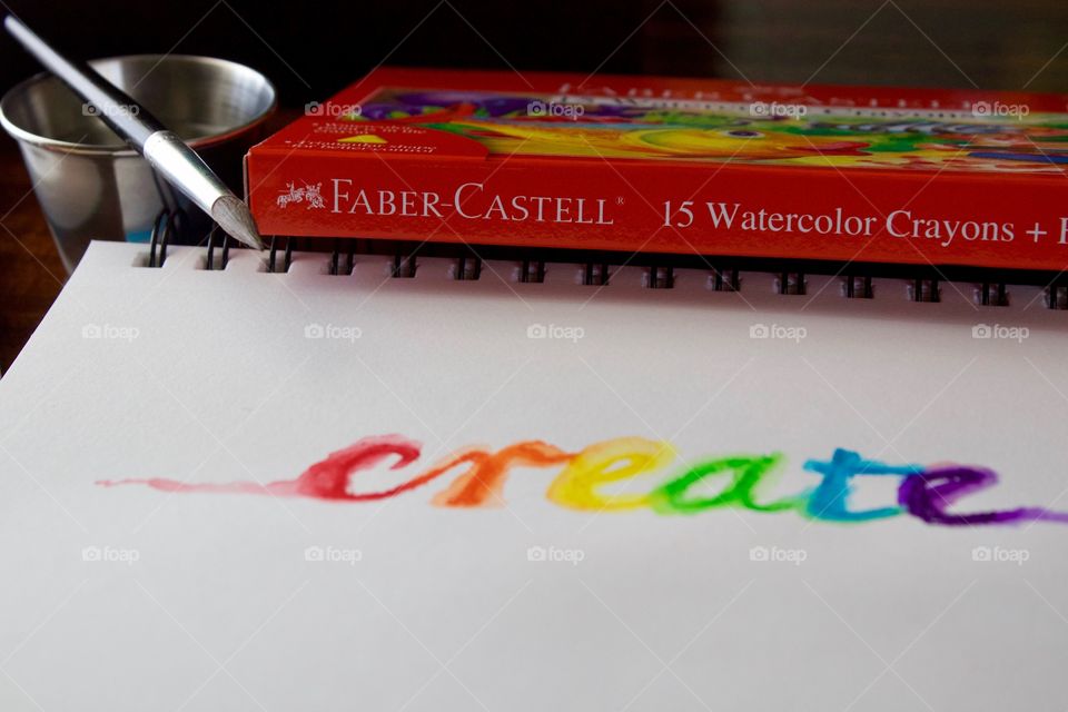 Colours of the World - watercolor crayon product box, watercolor brush and stainless steel water container, and the word “create” in rainbow colors on mixed media wire-bound paper