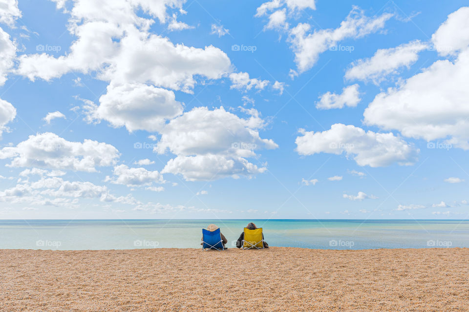 Couple sitting comfortably in a beach chairs admiring calm sea waters on sunny summer day.