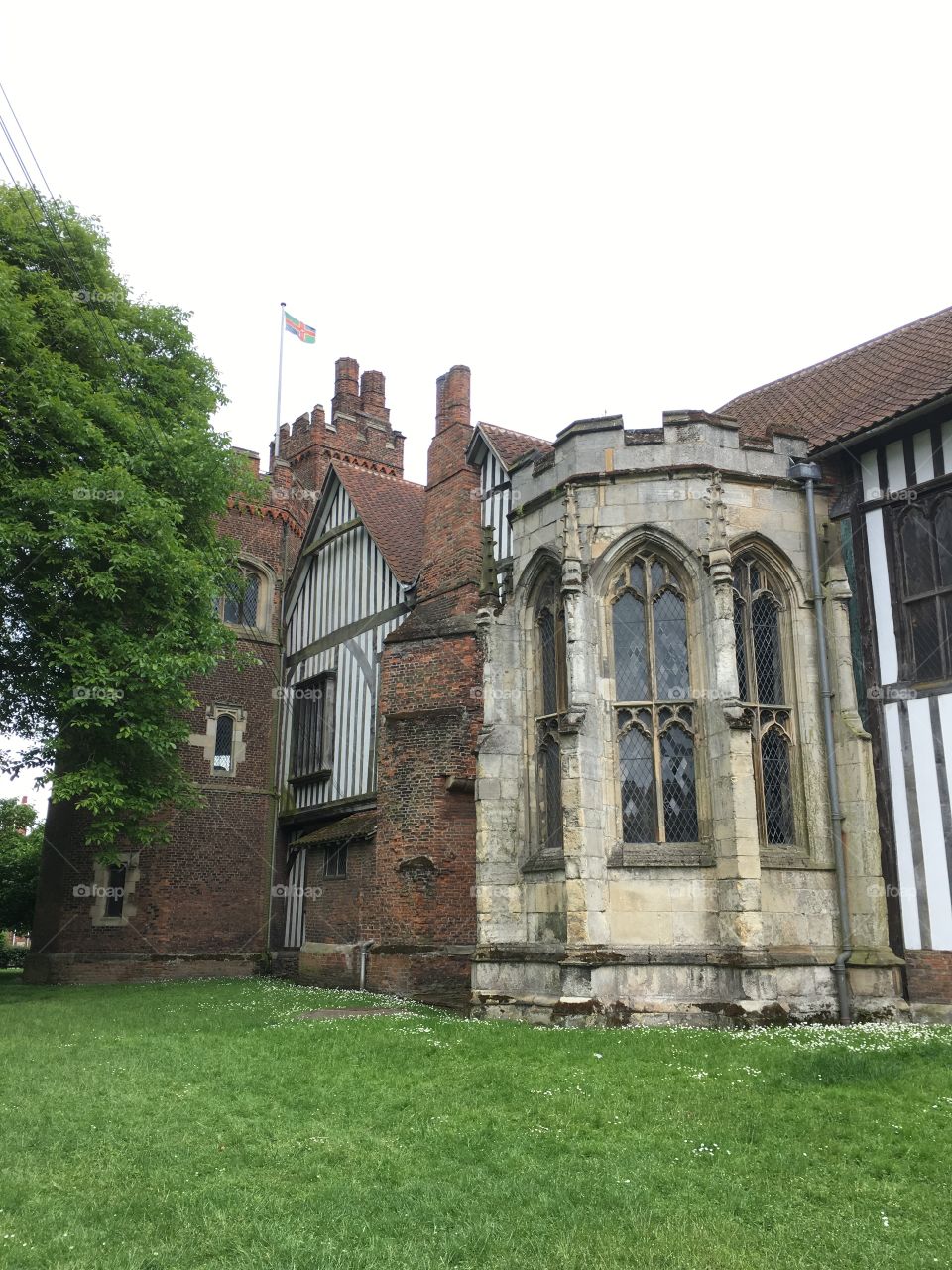 Exterior view of brickwork, timber framework and windows of the mediaeval Manor House of Gainsborough Old Hall in England with tower flying the Lincolnshire flag