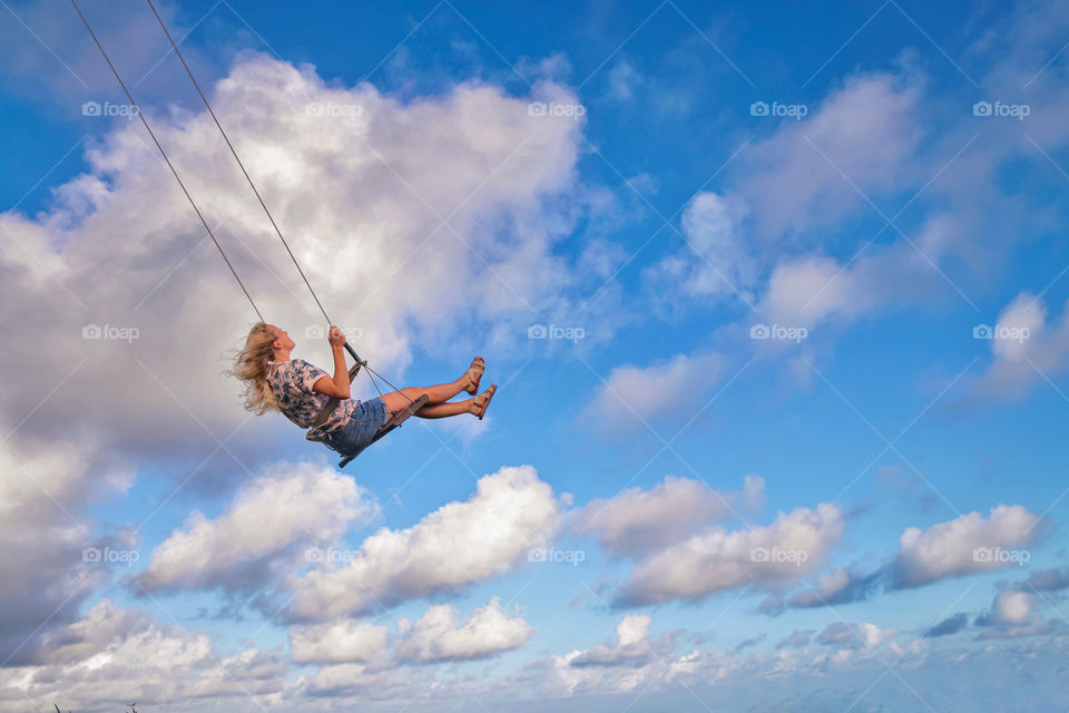 Blonde girl on a swing in the sky