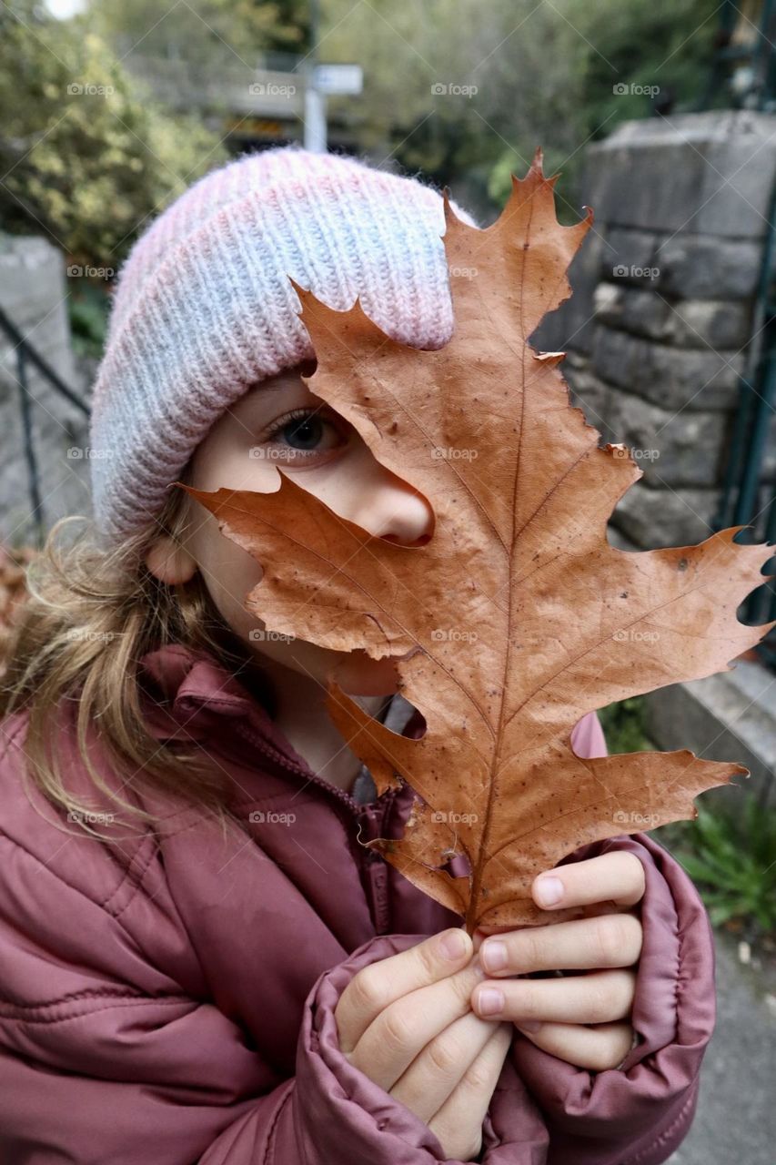 A girl looking behind big fall leaf