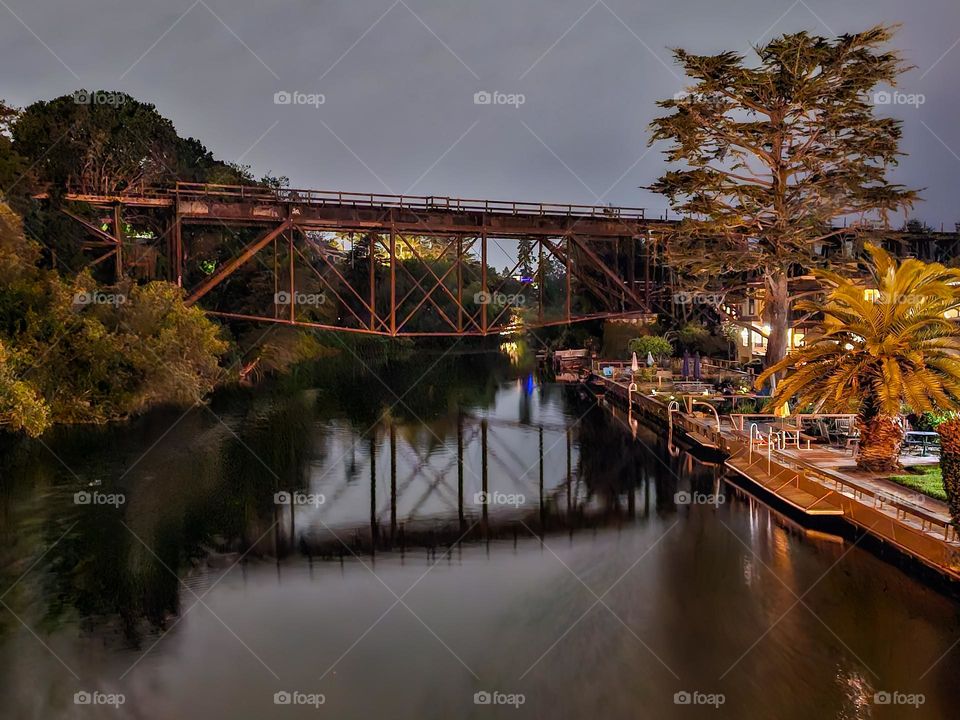 Old train trestle suspended over the Soquel River in Capitola by the Sea, California reflecting in the evening light with a soft cloudy sky 