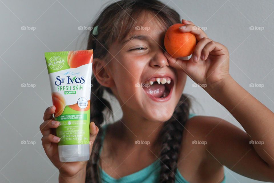 Happy little girl with an apricot and St.Ives skin care product in her hands