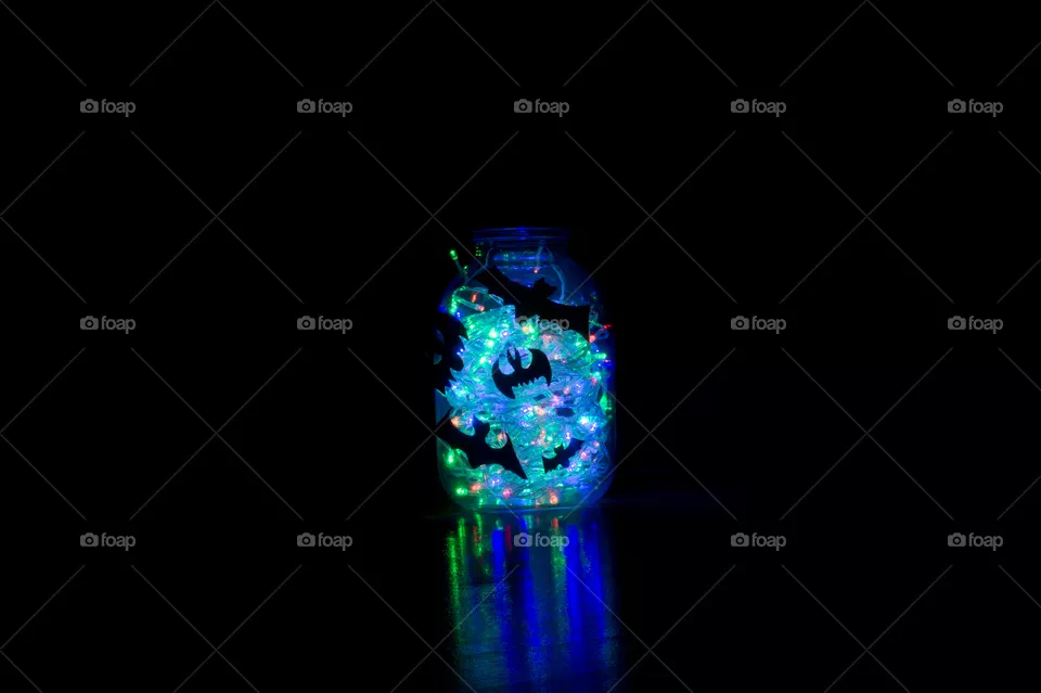 Halloween bats are glued to a glass jar with a garland glowing in it.