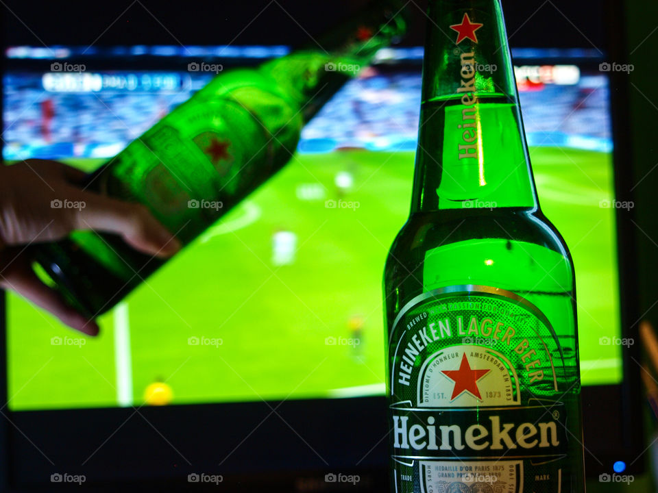 Heineken glass hand over, in the background football game.
