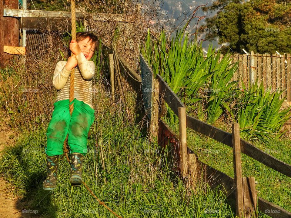 Boy On Rope Swing At Sunset. Childhood In The Golden Hour
