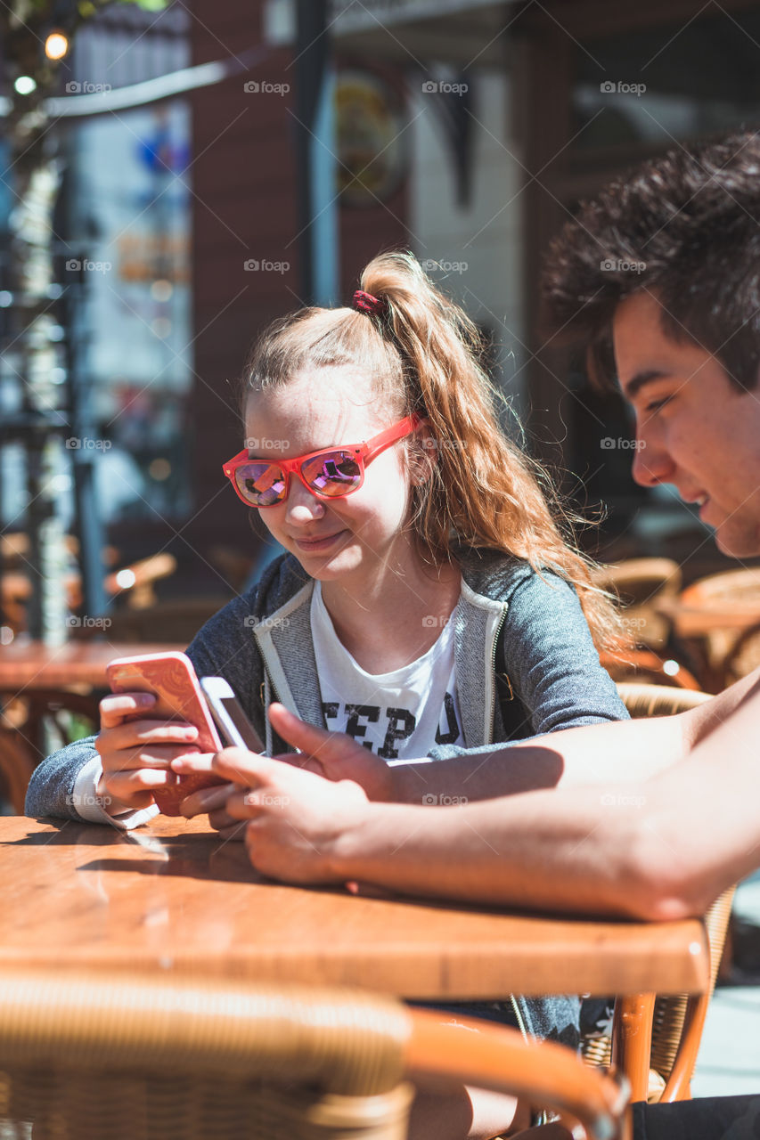 Young woman and man sitting in pavement cafe a the table talking and using mobile phones