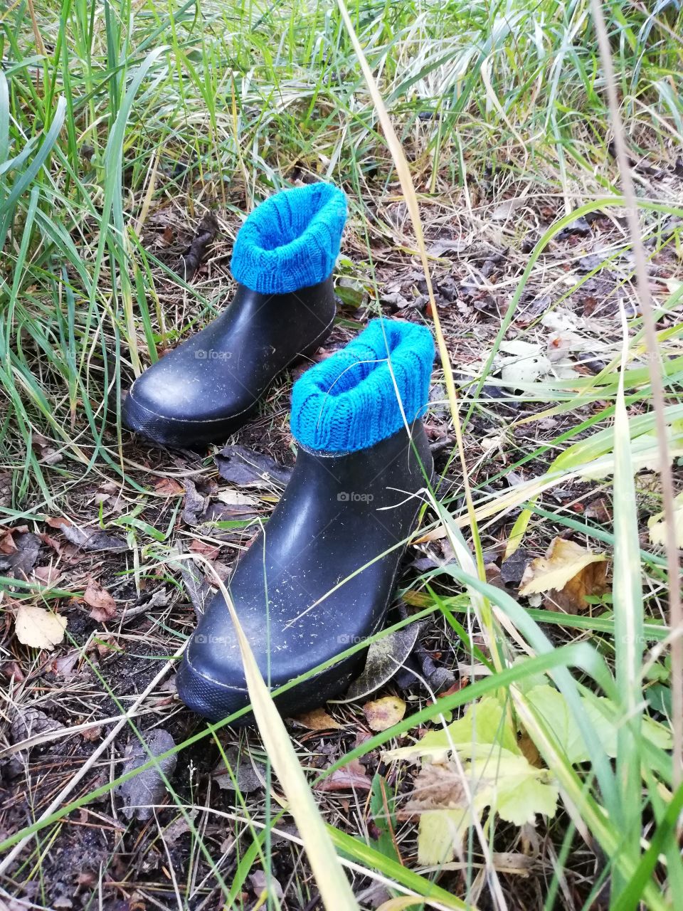 The black old fixed wellies along a path. The turquoise raised decorated woolen stockings, which edges turned on the shoes, which surfaces are dirty. Dry, fallen leaves of Autumn on the ground.