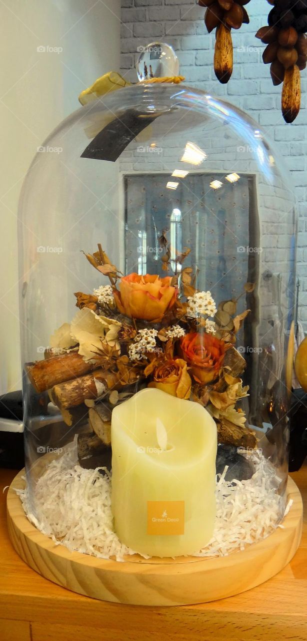 There are dried flowers and candle in the glass cover