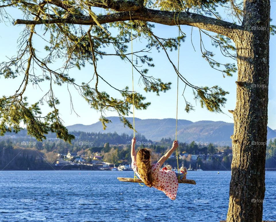 Girl swinging on tree swing in a scenic ocean paradise 