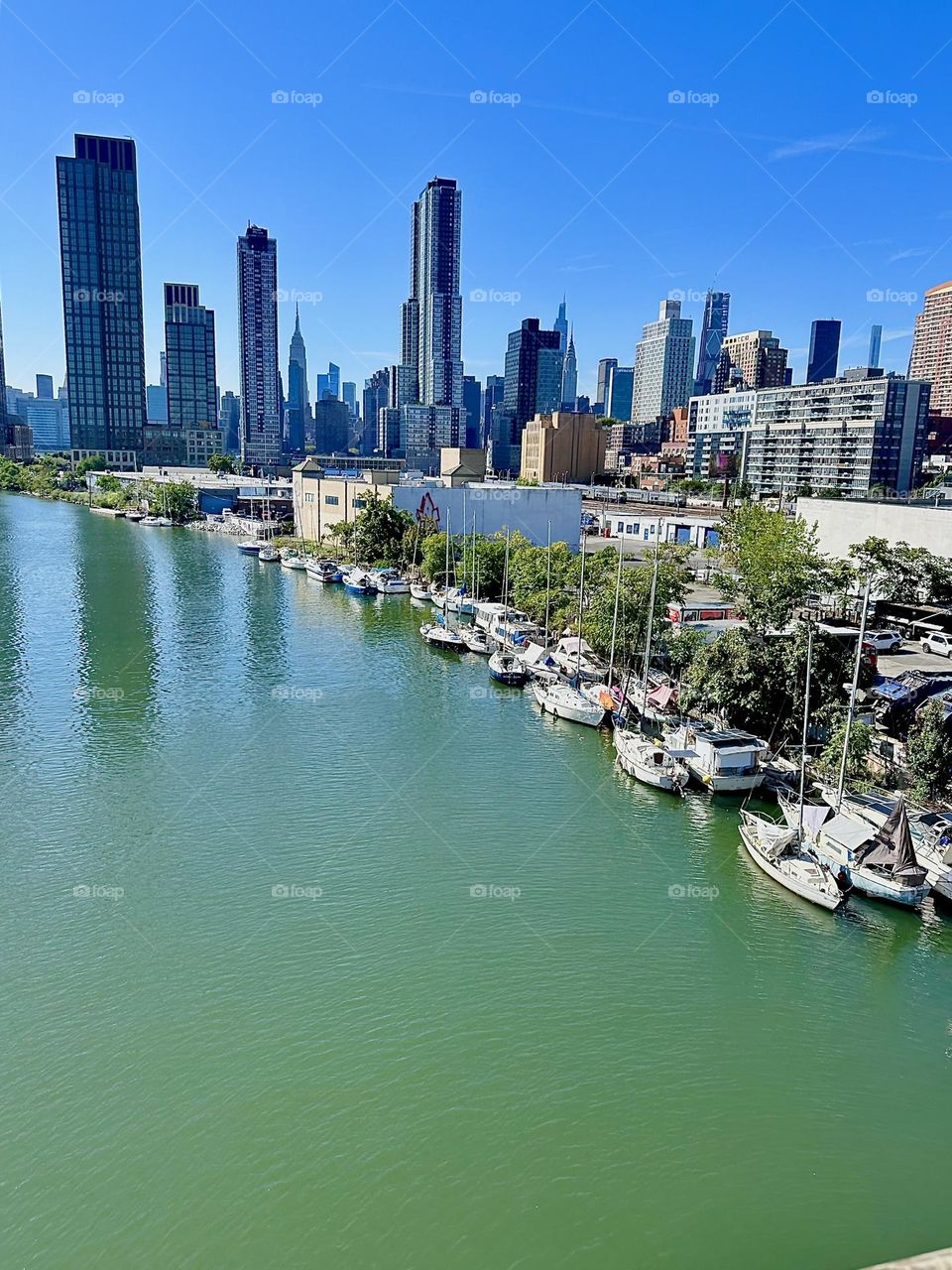 This is “Newtown Creek”, ocean inlet of the “East River” seen from the “Pulaski Bridge” that connects “Greenpoint”, Bklyn to LIC, Queens with its many boats. In the distance we see “Manhattan” incl. the “Empire State Bldg”. 2024. Hypnotic Productions