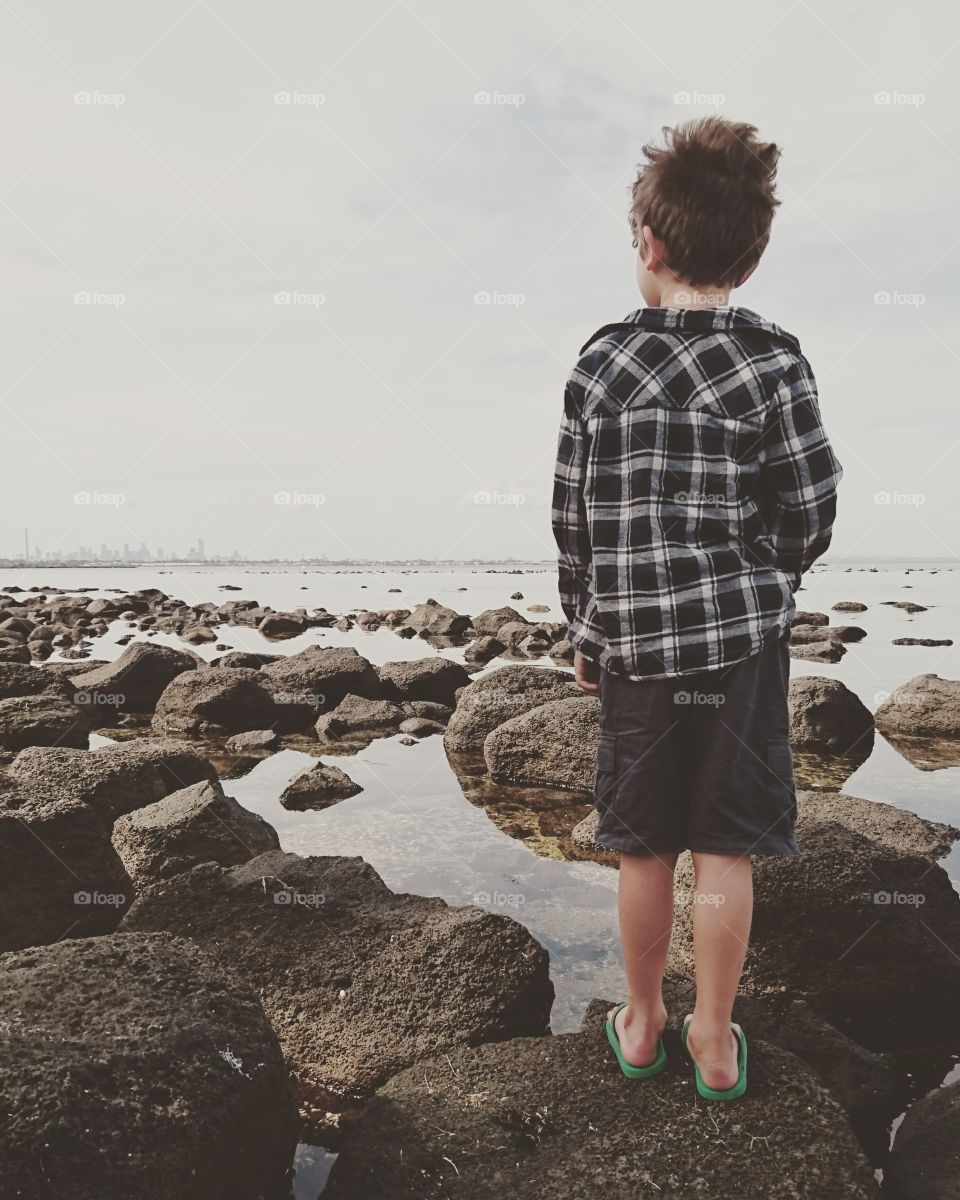 Rear view of a child standing on rock at beach