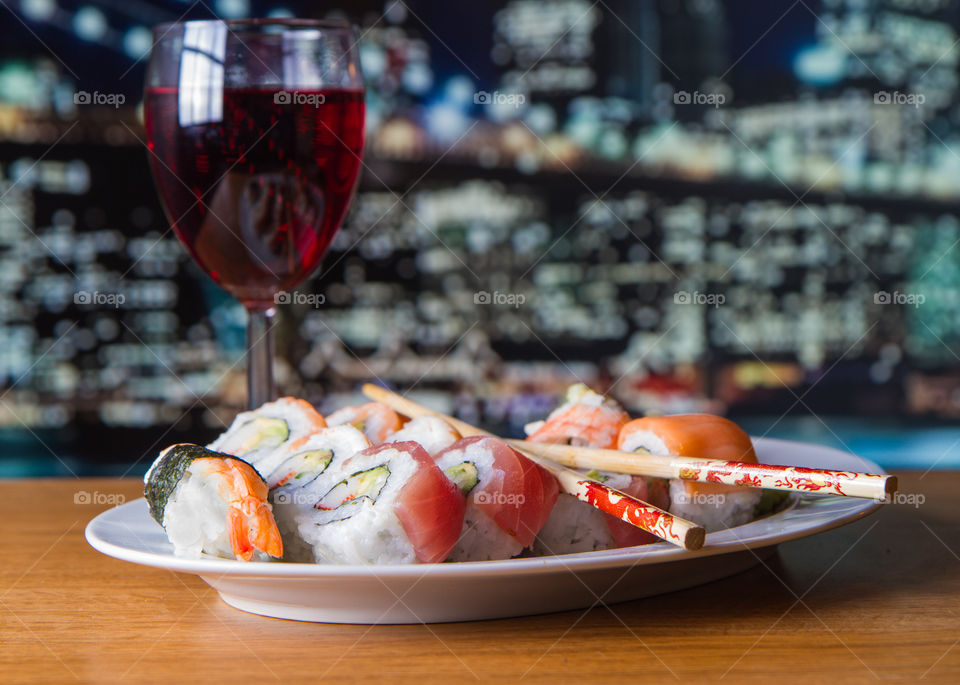 sushi rolls served on a white plate with red wine and a city view